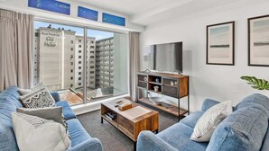 Una sala moderna con un conjunto de sofá, una mesa de centro y un televisor. Hay un ventanal con vistas a edificios.