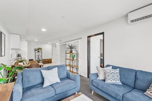A modern living room with two blue sofas, a coffee table, and a bookshelf. - 2BR Apt w/ Parking in Prime Spot by Zodiak Stays (Auckland)