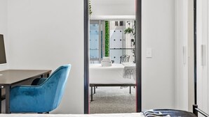 Habitación de hotel moderna con escritorio, una silla azul, cama y vistas al balcón y al área exterior.