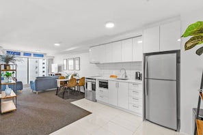 A modern kitchen with white cabinets, a stainless steel refrigerator, and a dining area with a table and chairs.