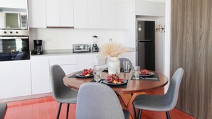 A modern kitchen with white cabinets, a microwave, a coffee maker, and a toaster. There is a dining table with two chairs, plates of fruit, and glasses of water. - Departamento exclusivo en Chapultepec 67 (Guadalajara)