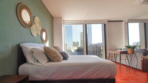 A modern hotel room with a large bed, a desk, and a balcony with a city view. - Departamento exclusivo en Chapultepec 67 (Guadalajara)