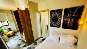 A hotel room with a large bed, a wooden wardrobe, a small seating area with a yellow chair, and a view of a building through a window. - Elegante loft urbano (Guadalajara)