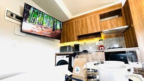 A modern kitchen with wooden cabinets, a coffee machine, a microwave, and a television displaying a forest scene. - Elegante loft urbano (Guadalajara)