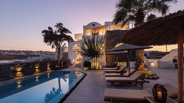 A poolside area with lounge chairs, a thatched umbrella, and a stone wall. - Santorini Garden Homes (Santorini)
