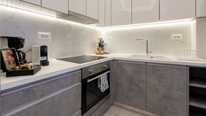 A modern kitchen with white cabinets, a black oven, a sink, and a countertop with a coffee machine and a picture frame. - Santorini Garden Homes (Santorini)