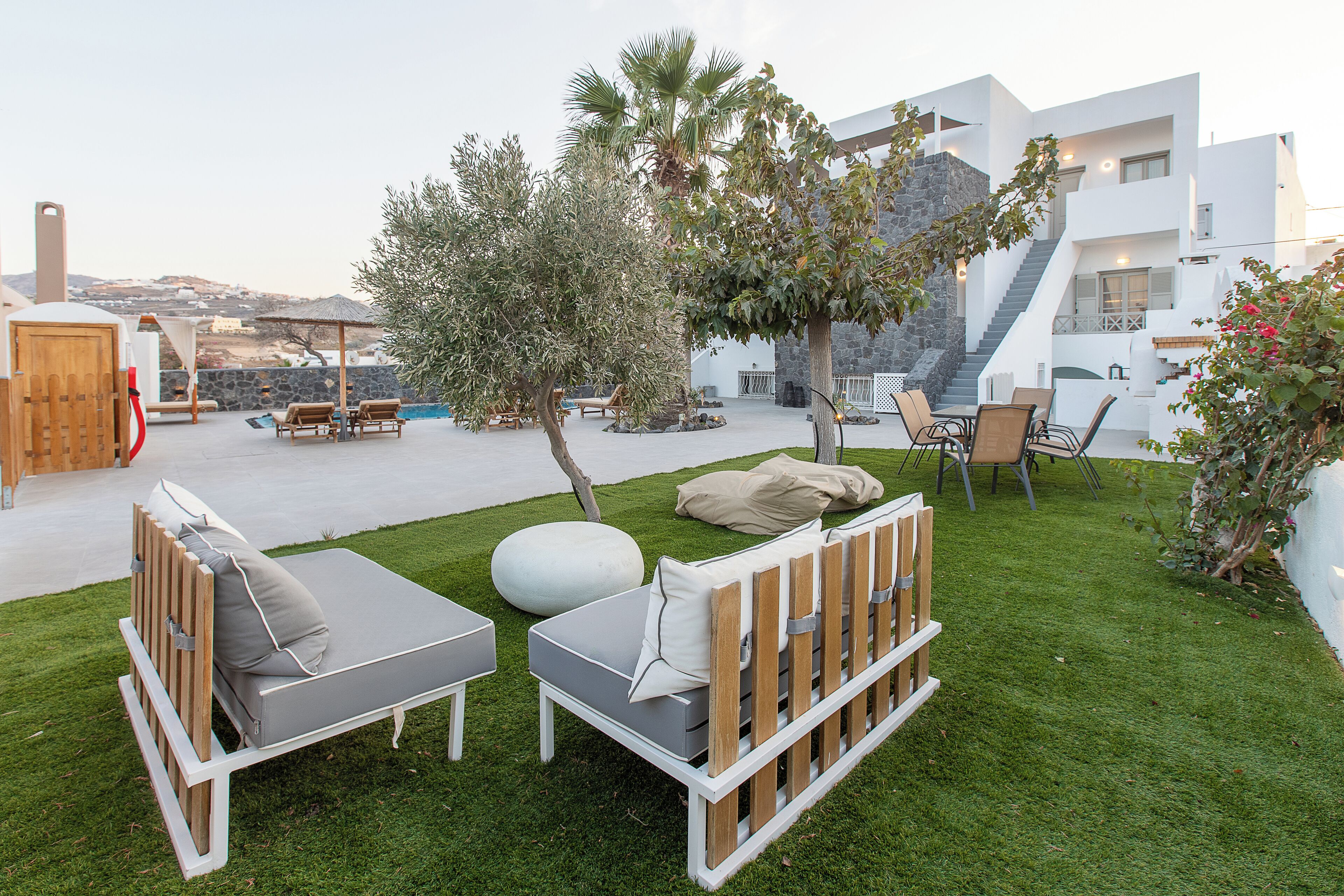 Un área de estar moderna al aire libre, con sillones reclinables y una pequeña mesa, rodeada de un césped cuidado y un muro de piedra.