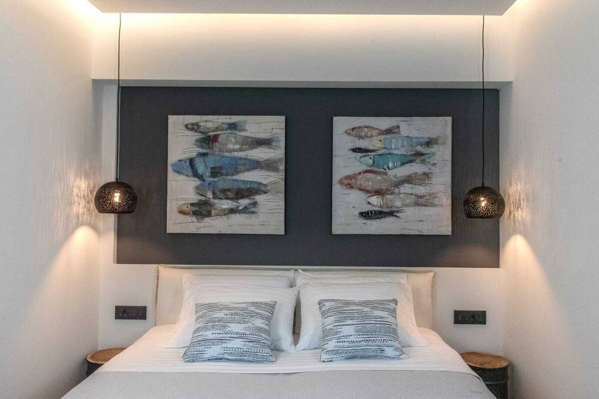 A bedroom with a bed, two wall-mounted paintings, and two pendant lights.