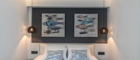 A bedroom with a bed, two wall-mounted paintings, and two pendant lights.