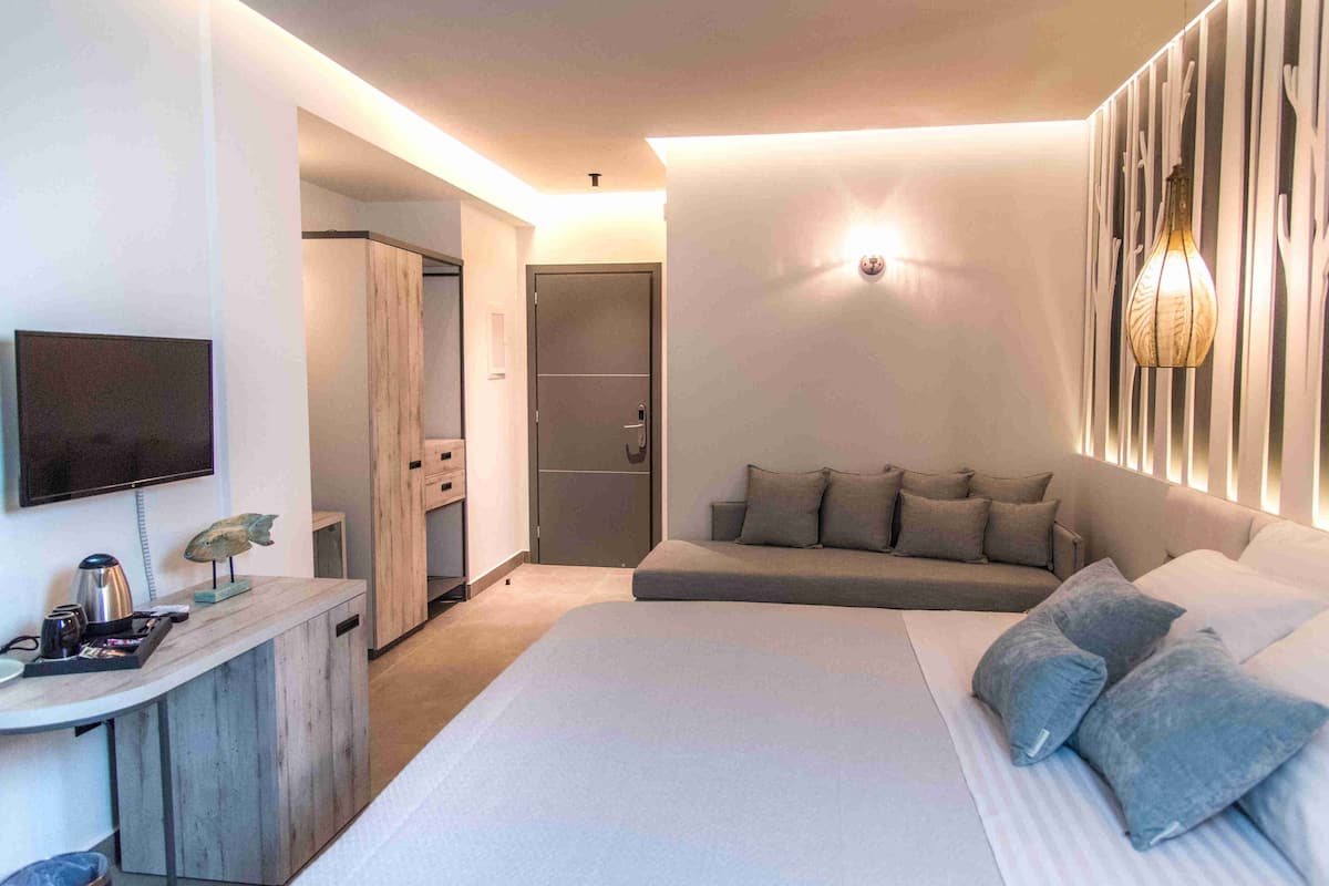 A modern hotel room with a large bed, a sofa, a TV, a desk with a kettle, and a wardrobe.