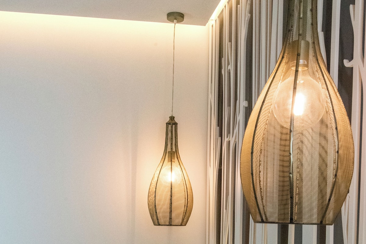 A neatly made bed with white and gray pillows, a hanging light fixture, and a wall with vertical slats.