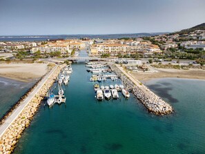 An aerial view of a marina with boats docked, a bridge connecting to the mainland, and surrounding residential buildings.
