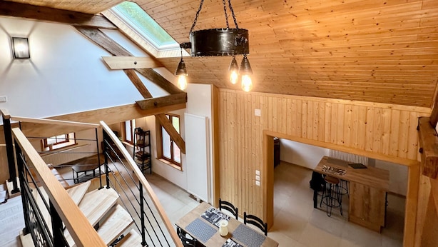 A spacious loft-style room with a high ceiling, exposed wooden beams, a mezzanine level, and a dining area. - Quiet Vosges Cottage for 4 with Terrace and Children's Area (Le Saulcy)