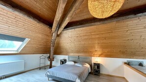 A bedroom with a sloped ceiling, a skylight, a bed, bedside tables, and a hanging light fixture. - Quiet Vosges Cottage for 4 with Terrace and Children's Area (Le Saulcy)
