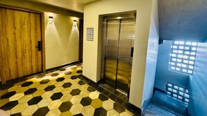 A hallway with a checkered floor, an elevator, and a door with a wooden finish.