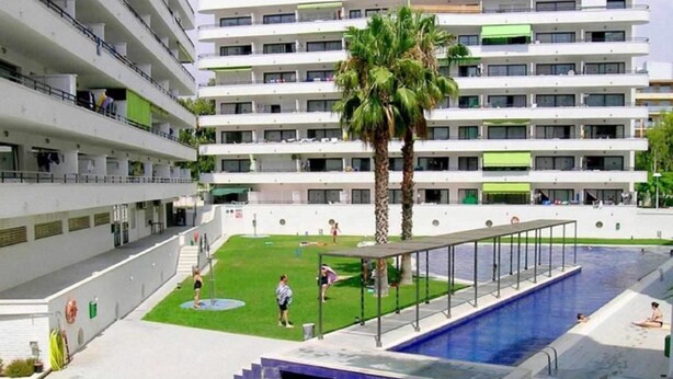 Un edificio moderno de varios pisos, con un patio central que tiene una piscina y palmeras.