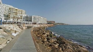 Un sendero costero que lleva a un hotel frente a la playa, con varios balcones y un litoral rocoso.