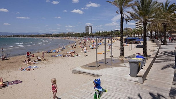 Ein Strand mit einer Holzpromenade, Palmen und blauem Himmel.