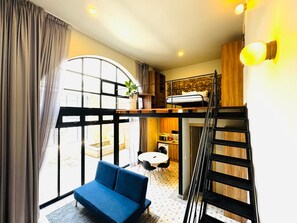 A compact room with a bunk bed, a blue sofa, a small dining table, and a kitchen area.