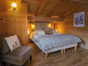 A cozy wooden cabin bedroom with a bed, bedside lamps, a chair, and a poster on the wall.