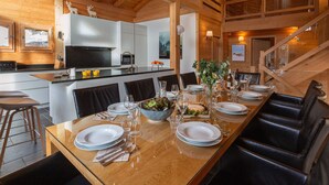 A modern kitchen with wooden beams, a dining area with a long table set for six, and a staircase. - 4★ Chalet, 12 pers, spa, panoramic view, near shuttle (La Clusaz)