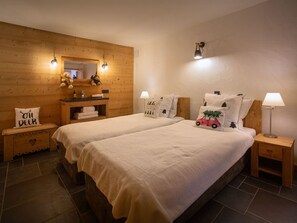 A cozy room with two beds, a wooden wall, a small bathroom, and a nightstand with a lamp.