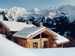 A wooden chalet with a sloped roof, surrounded by snow-covered mountains. - 4★ Chalet, 12 pers, spa, panoramic view, near shuttle (La Clusaz)