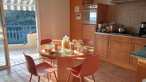 A dining area with a round table, four chairs, a kitchen with a stove and cabinets, and a balcony with a railing.