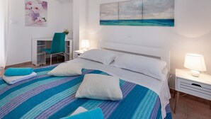 Ein Hotelzimmer mit einem großen Bett, einem Schreibtisch und einem Sessel. An den Wänden hängen zwei Bilder.