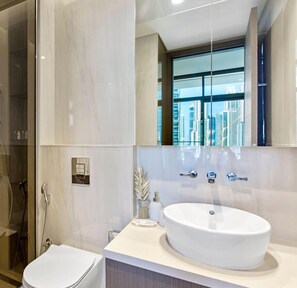 A modern bathroom with a large mirror, a round sink, and a toilet.