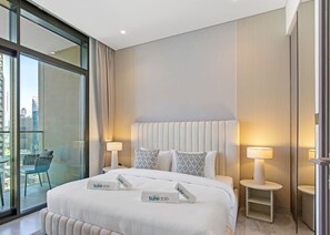 A hotel room with a large bed, two bedside tables with lamps, a view of the city through floor-to-ceiling windows, and a balcony with a chair.