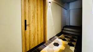 Un pasillo con puerta de madera, una lámpara encima y una escalera con suelo de baldosas.