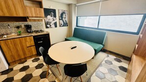 Cocina compacta con comedor, sofá verde y ventana con persianas.