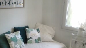 A bedroom with a bed, pillows, a small white chair, and a window with blinds.