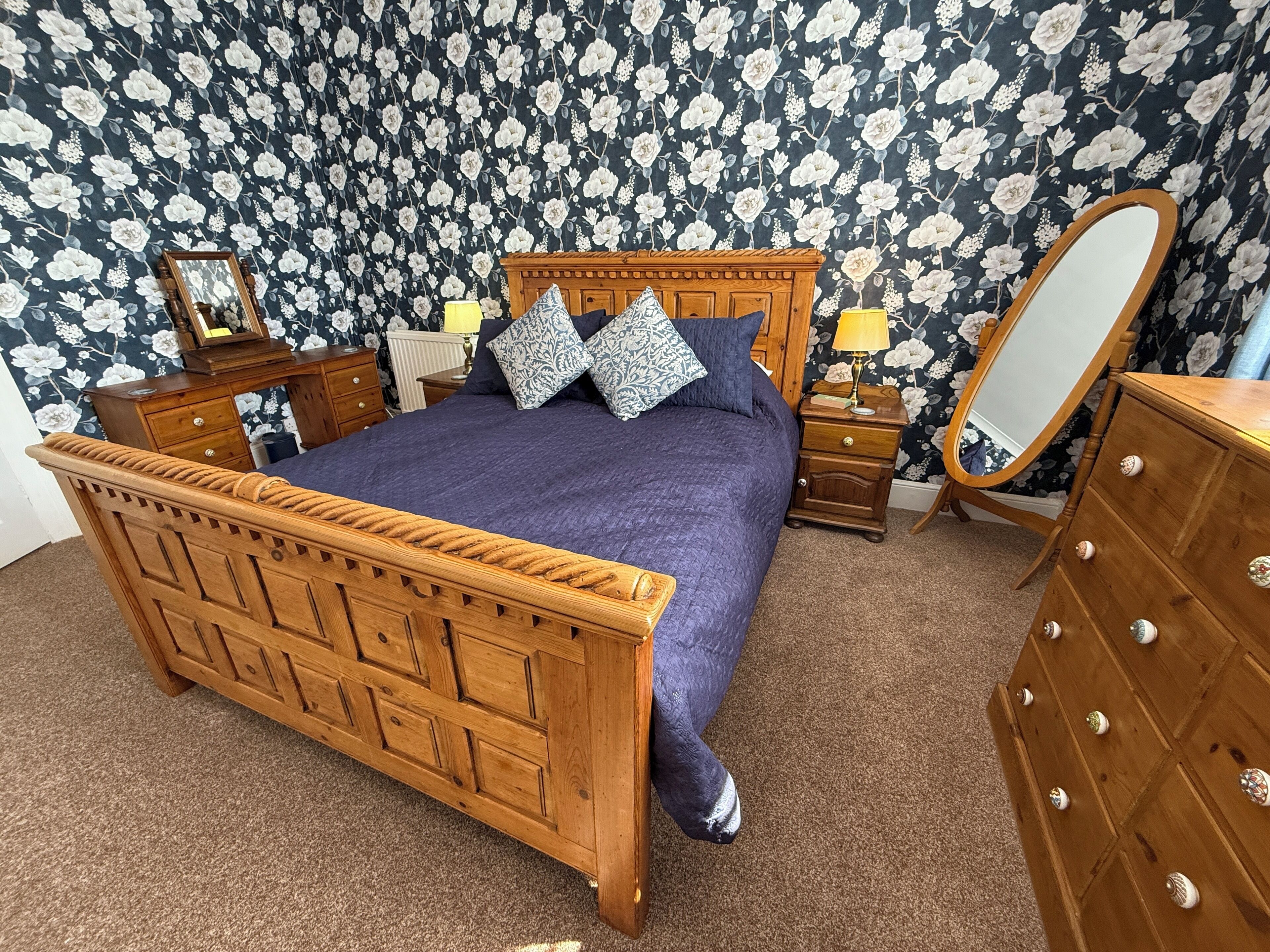 A bedroom with a wooden bed, a nightstand with a lamp, a dresser, and a mirror.
