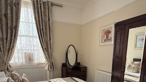 Makuuhuoneessa on suuri sänky, lipasto, peili ja ikkuna, jossa on verhot.