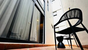 A patio area with a black chair and a table, a sliding glass door, and a tiled floor. - Elegante loft urbano (Guadalajara)