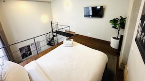 A hotel room with a bed, a TV mounted on the wall, a staircase, and a potted plant. - Elegante loft urbano (Guadalajara)