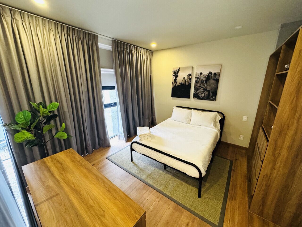A modern bedroom with a bed, a wooden desk, a plant, and a wardrobe.