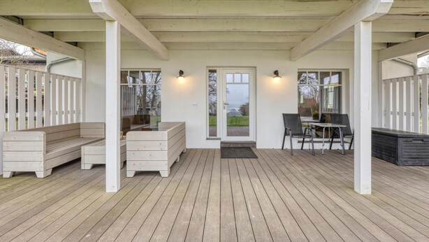 A covered porch with a wooden deck, white columns, a door with glass panels, and two tables with chairs. - Amazing apartment in Klein Upahl with lake view (Klein Upahl)