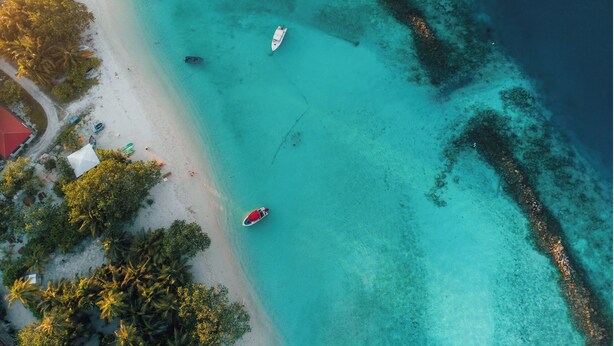 An aerial view of a beach with clear turquoise waters, several boats, and a small building with a red roof. - Enchanting bed & breakfast with WiFi & AC in vibrant Thulusdhoo Coke Surf break (Thulusdhoo)