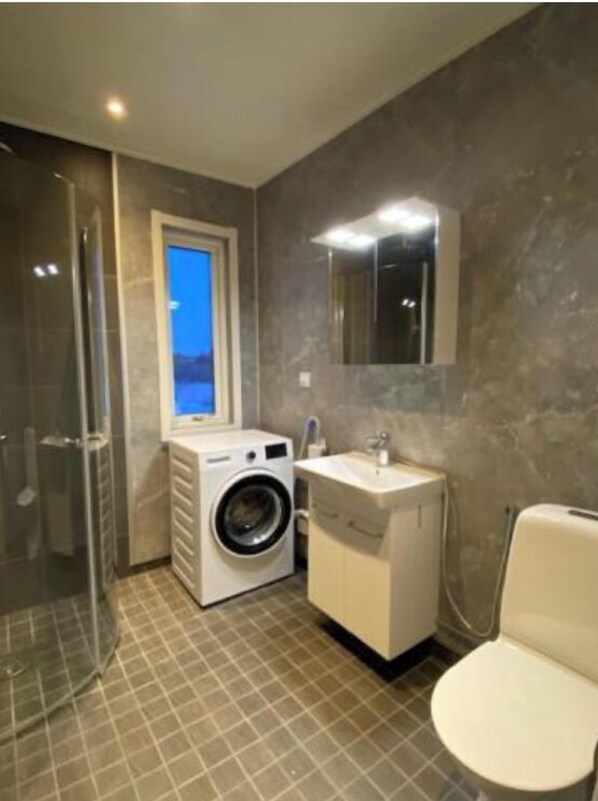 Een moderne badkamer met een glazen douchecabine, een ingebouwde wasmachine, een wastafel en een toilet.