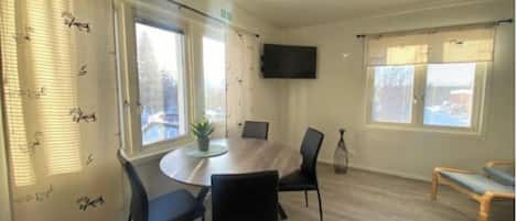 A conference room with a round table, black chairs, a potted plant, and a TV on the wall.