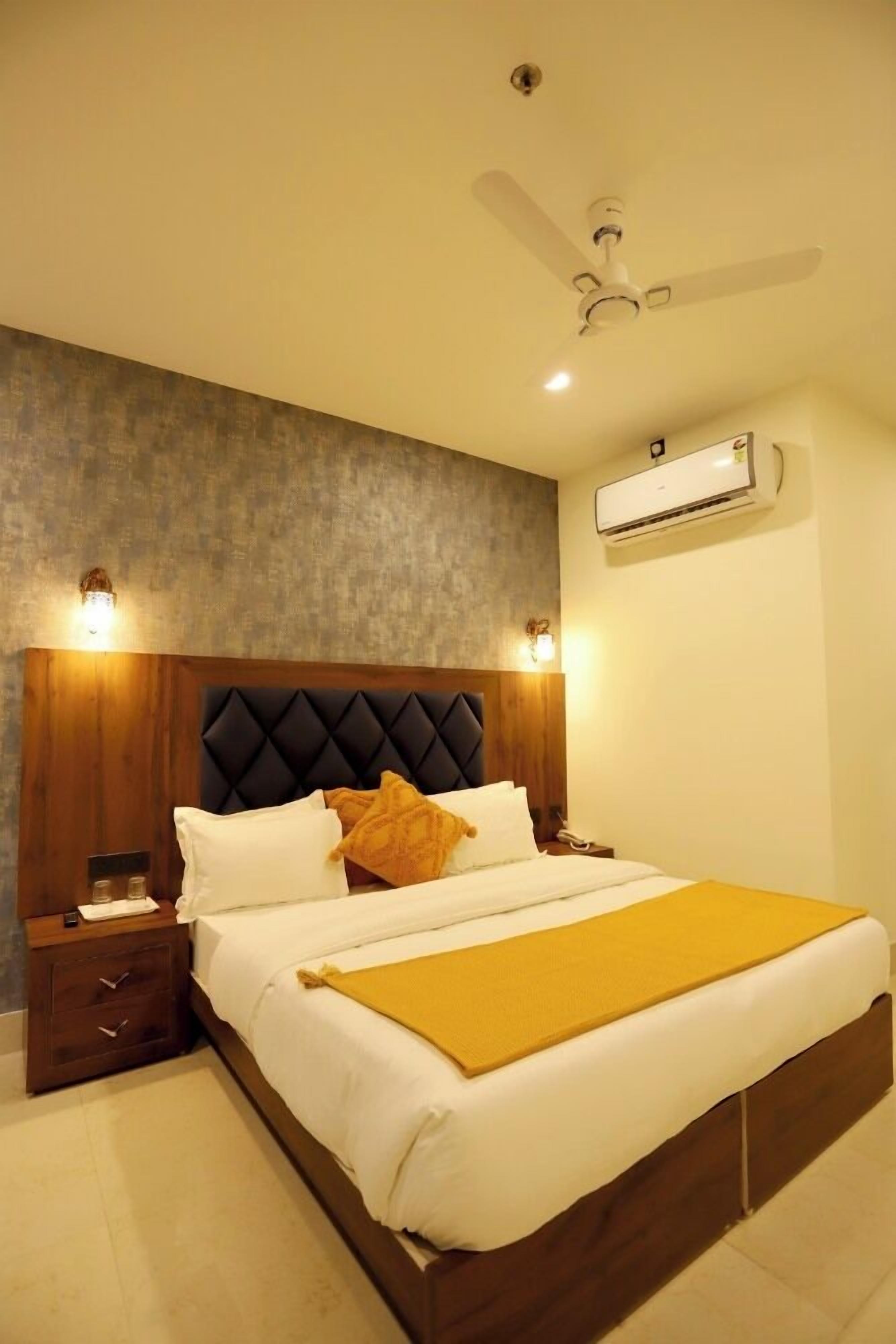 Ein Hotelzimmer mit Bett, Nachttisch, Wandklimaanlage und Deckenventilator.