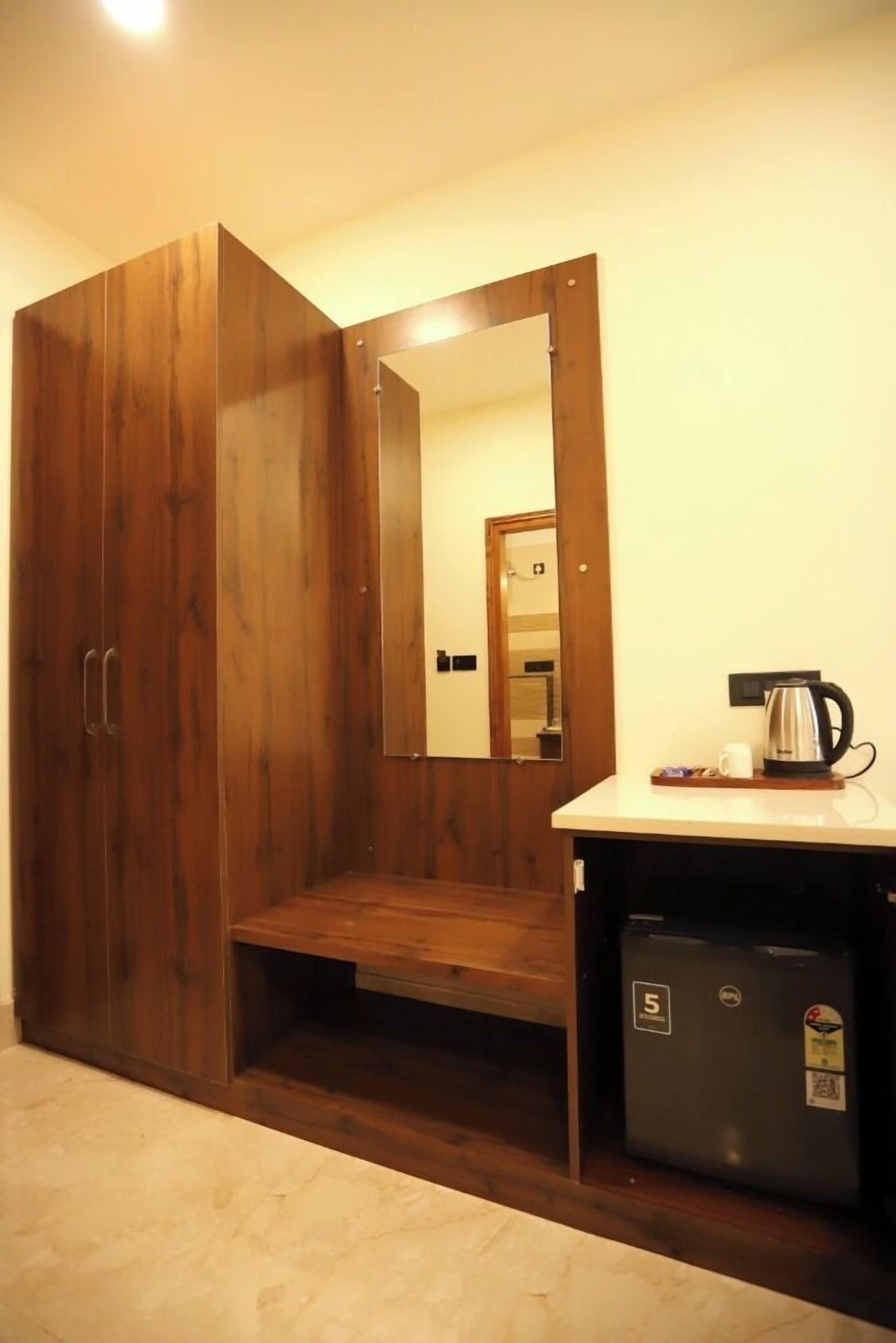 A room with a wooden wardrobe, a mirror, a small kitchenette with a coffee maker, and a refrigerator.