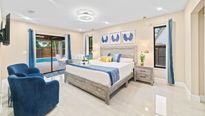 A modern bedroom with a large bed, a bedside table, a chair, and a view of a pool. - Grand Lux Villa /Heated Pool/Spa/Game fun/Nr Beach (Lantana)