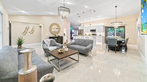 A spacious living area with a modern chandelier, grey sofas, and a dining table. - Grand Lux Villa /Heated Pool/Spa/Game fun/Nr Beach (Lantana)