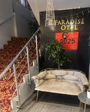 A staircase with red carpet, a cushioned seating area, a sign reading "Paradise Hotel 2025", and a decorative plant. - paradiseotel (Erzurum)