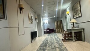 Een hal met een kamerbreed tapijt, een bank, een tafel met een lamp en kunstwerken aan de wanden.