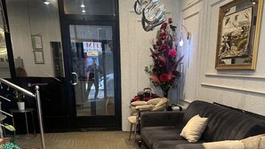 Een moderne hotellobby met een donkergroene bank, een kleine tafel met een bloevas, en een ingelijste foto aan de muur.